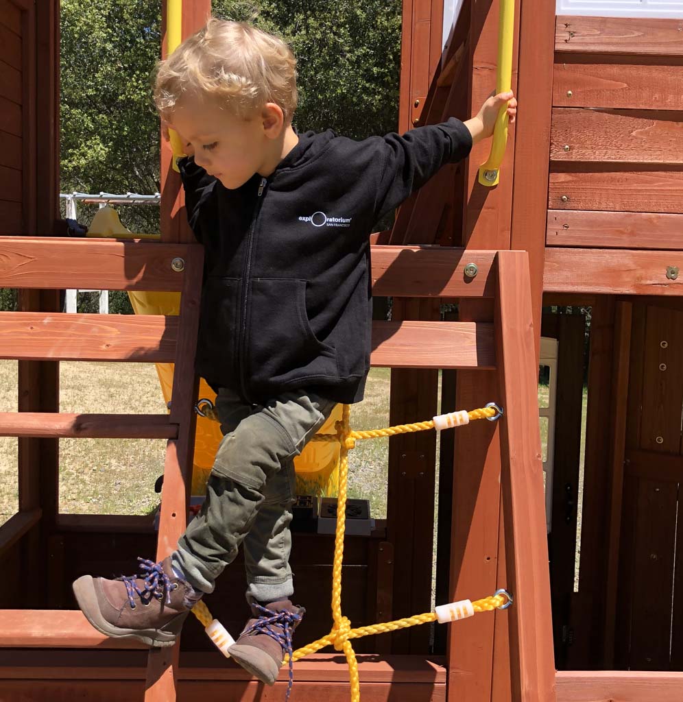 Toddler on playset wearing a black hoodie with Exploratorium on the front in white.