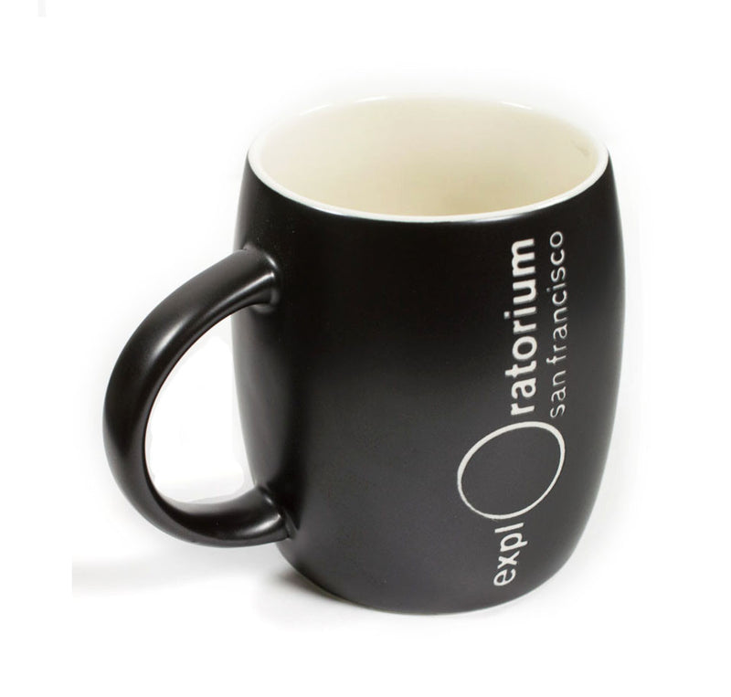 It is a black ceramic mug with the Exploratorium logo, San Francisco, vertically etched in white. The inside of the mug is white.