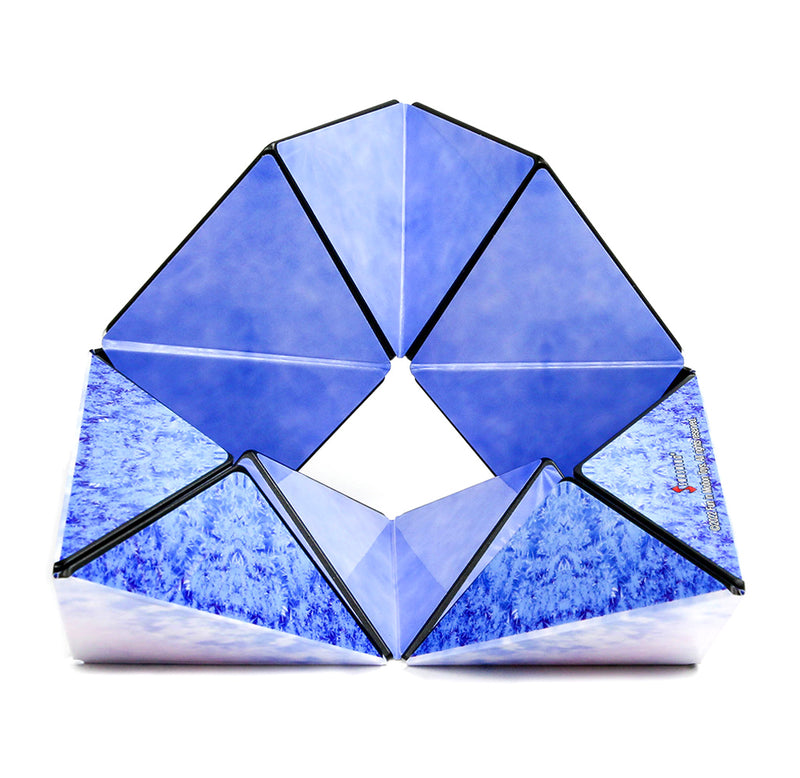The polar Shashibo is set up in a round curvature design with three sides showing different aspects of a polar region, freezing ice, and blue holographic snowflakes against blue in white and pink.