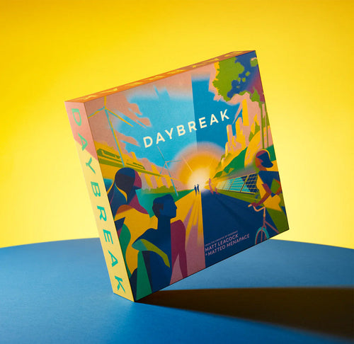 A square box with colorful artwork on the front cover depicting people, buildings, wind mills, solar panels, and a sun in the center. The box is tilted on its corner on a blue table with a yellow background. 