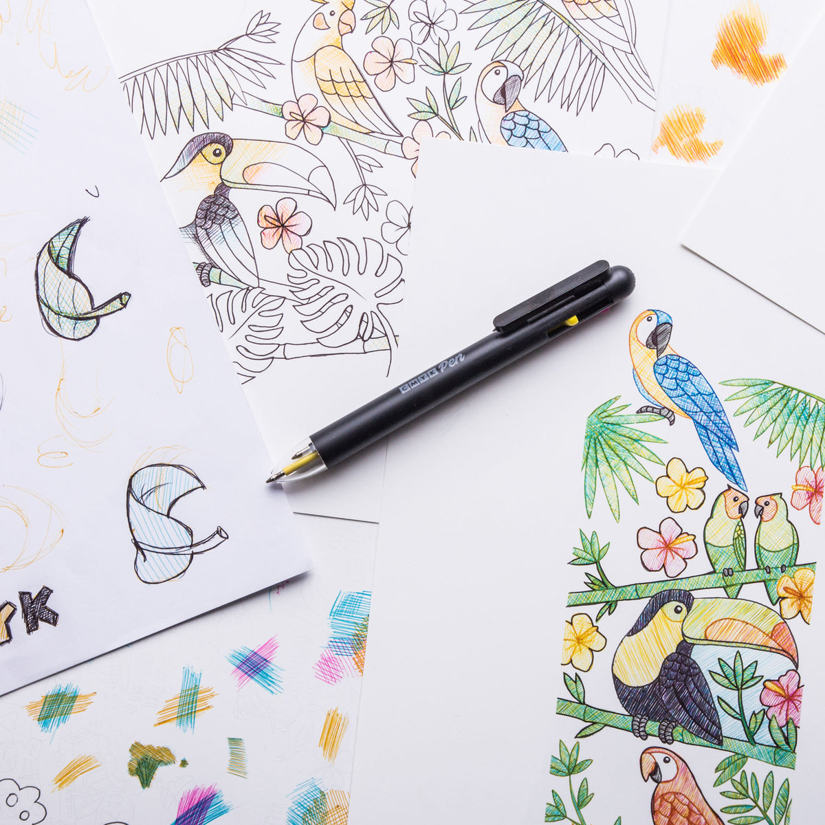 CMYK pen on top of scattered papers with drawings.