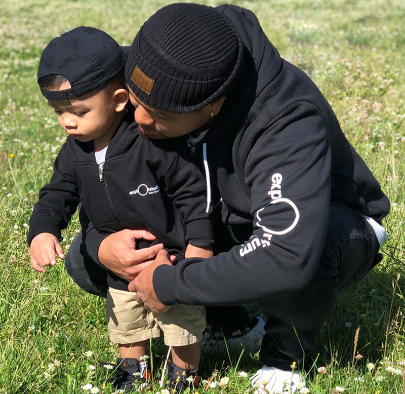 Father holding his son while they are both wearing black hoodies with the Exploratorium logo in white.