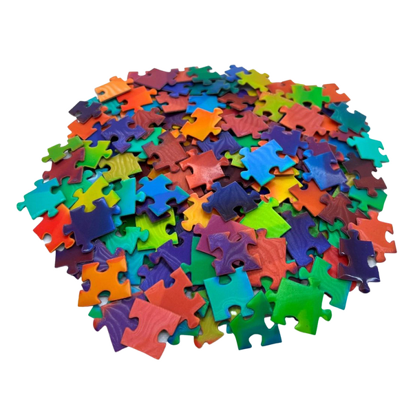 A pile of colorful jigsaw puzzle pieces in a rainbow of colors, photographed on a clean white background.