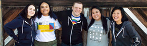 Five people stand together in the Exploratorium apparel; blue, black, and gray hoodies, a white periodic table shirt, and a gray Tinkering shirt are featured.