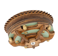 Close-up of an ornate carved wooden object with layered ridges, scalloped edges, mint-green inlays, brass studs, and curved wood details.