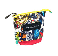 A zippered cosmetic pouch featuring a vibrant multicolor butterfly print on a white background, with a solid red bottom base, a black brand label reading 'COGNITIVE SURPLUS', and a bright yellow zipper.