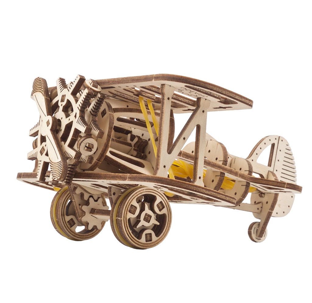 3/4 front view of the Biplane model kit. The model is an open design with the inner pieces visible from the exterior. Rubber bands lace around the wheels and through the body of the wooden model plane.