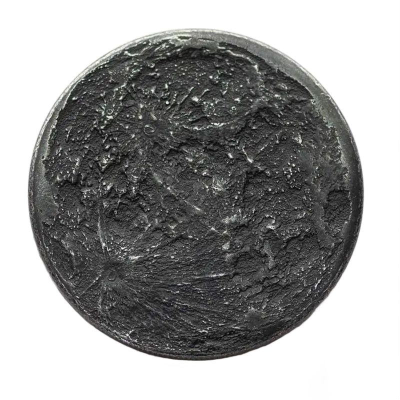 A round black iron coin with a highly detailed, textured lunar surface design featuring craters and shadows, isolated on a white background.