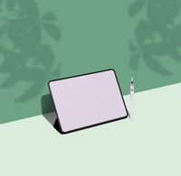 A minimalist digital tablet with a black bezel and stand, shown at an angle on a split green and pale green background, next to a slim white paintbrush stylus.