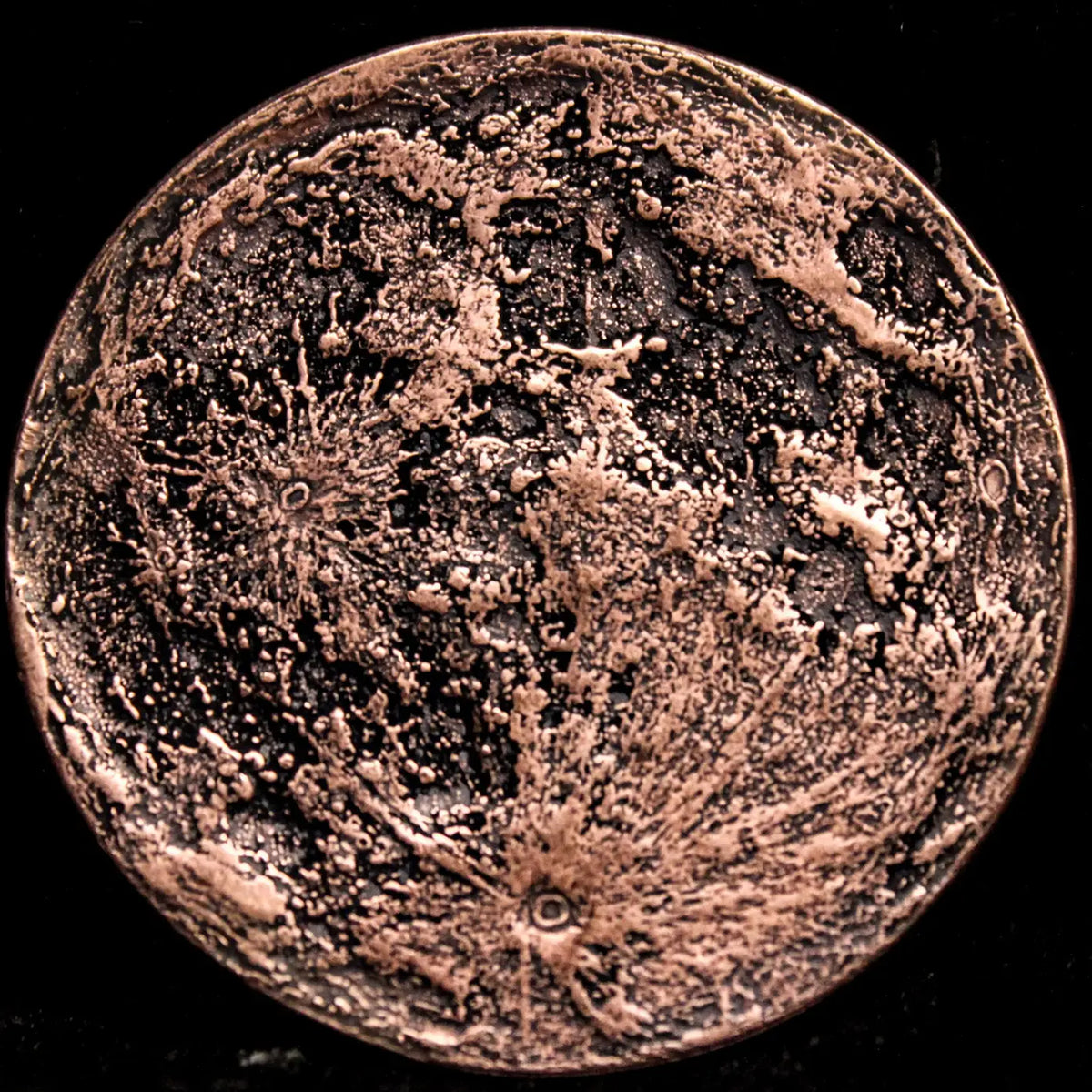 A circular copper-colored metal coin featuring a textured, cratered moon or planetary surface design, shown against a solid black background.