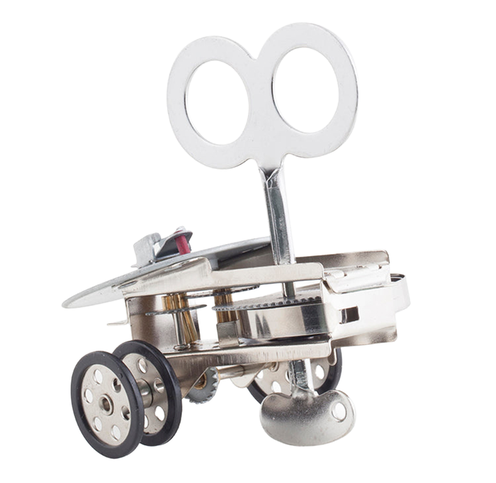Close-up of a shiny metal wind-up toy with a butterfly key, gears, wheels, and a curved resonator on white.