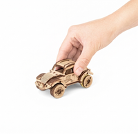A hand gently holds a small wooden toy race car with detailed wheels and the number 56, isolated on a white background; playful, calm tone.