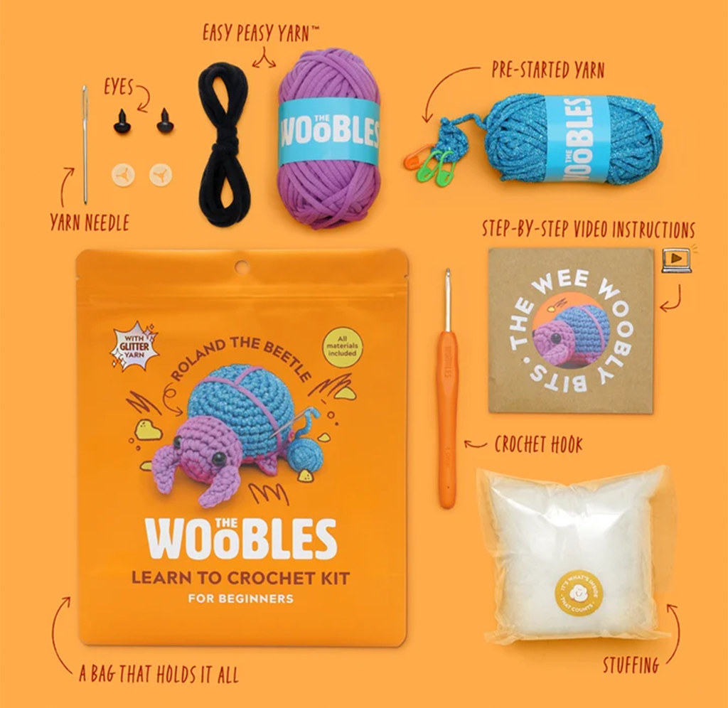 An orange-background beginner crochet kit display with purple yarn, blue pre-started yarn, eyes, needle, crochet hook, stuffing, instructions, and illustrated kit bag.