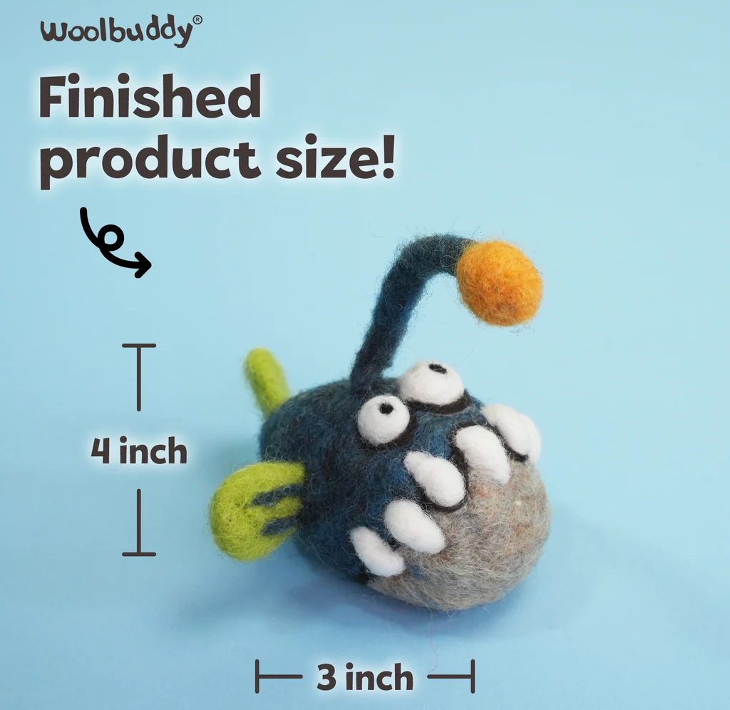 Woolbuddy felted blue-gray monster toy with white eyes, teeth, lime-green accents, and an orange-tipped antenna; finished size is 4 by 3 inches.