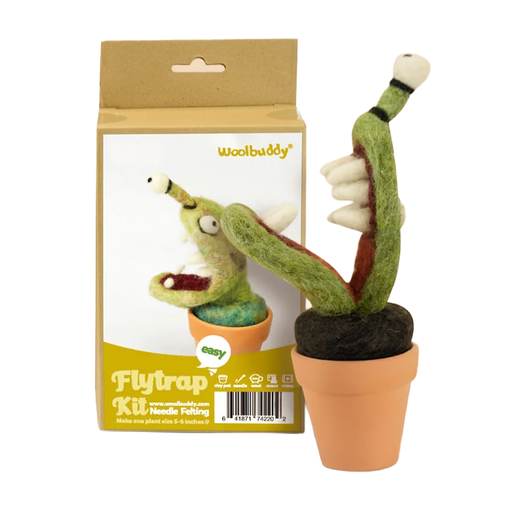 A whimsical green felt Venus flytrap with toothy jaws sits in a terracotta pot beside its Woolbuddy needle-felting kit box on a white background.