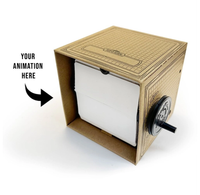 A cardboard animation viewer with a white screen and side hand-crank sits on a white background; an arrow points inside, suggesting a playful DIY invention.