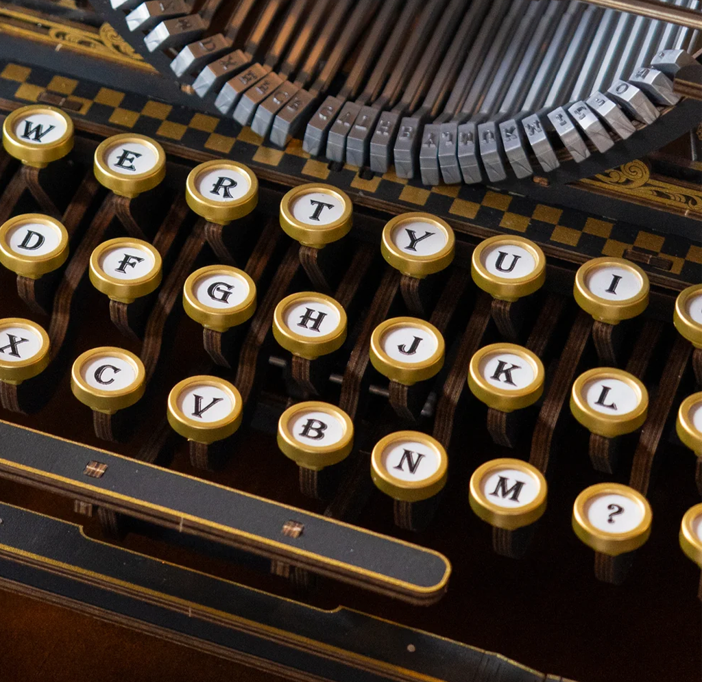 Close-up of an ornate antique typewriter with round gold-rimmed keys, black-and-white letters, and exposed metal type bars, evoking craftsmanship and nostalgia.