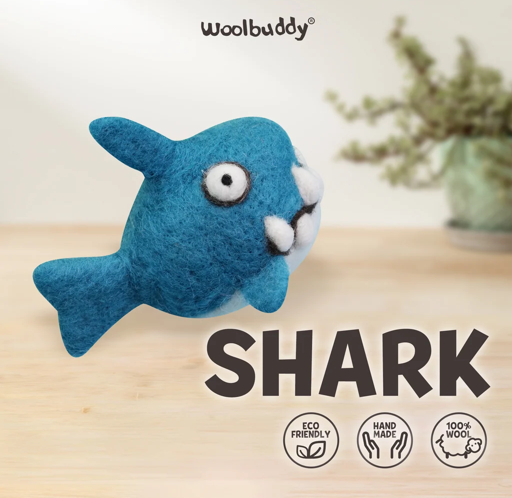 A playful blue wool-felt shark toy with big eyes and white teeth floats above a wooden surface; product text highlights eco-friendly, handmade, 100% wool.