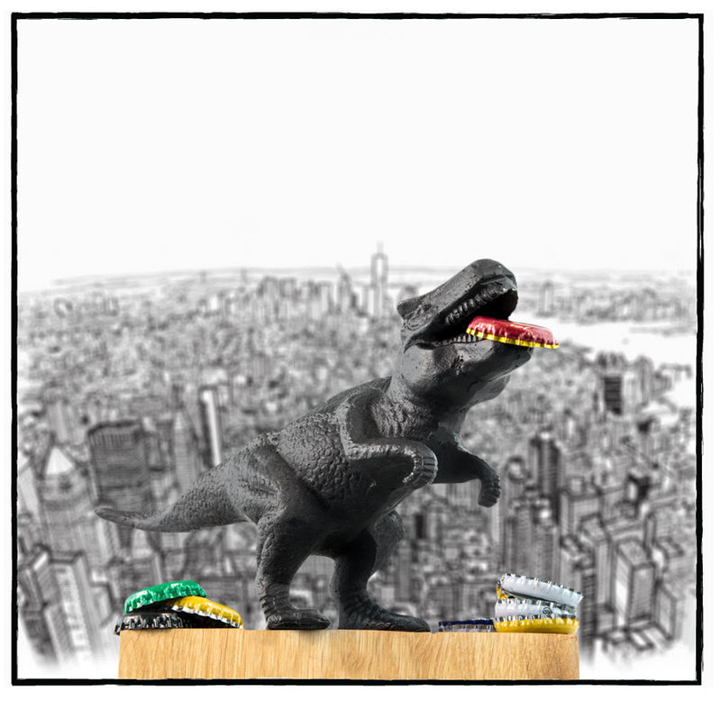Dinosaur bottle opener is posed in front of a black and white sketch of a metropolitan city with bottle caps in its mouth and scattered around its feet.