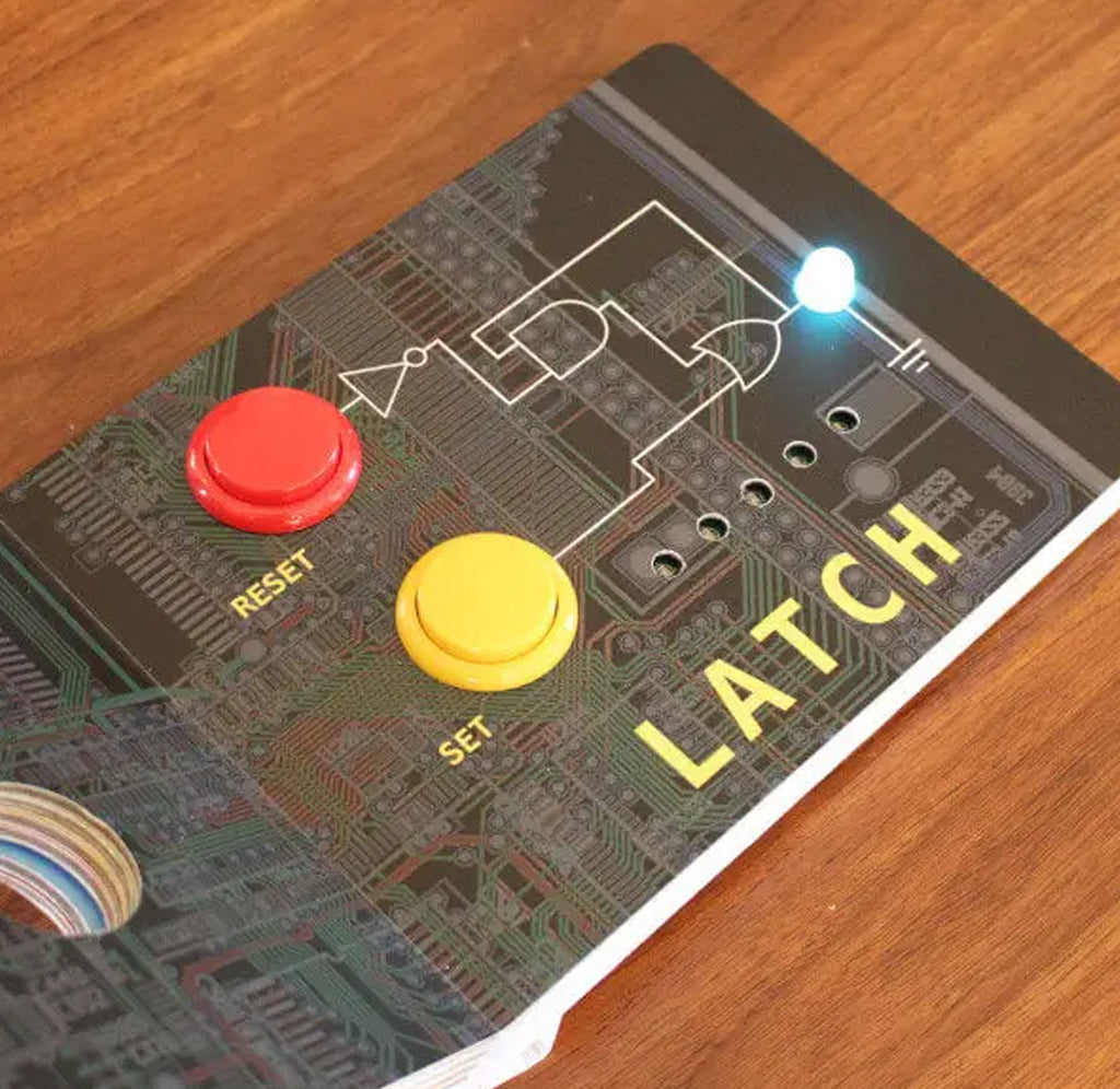A layout page from Engineering for Babies opened to page with 'LATCH' with a printed circuit board design, featuring a red button marked RESET, a yellow button marked SET, and a glowing blue LED on a wooden surface.