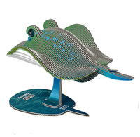 A 3D cardboard puzzle kit of a stingray assembled on a blue stand, featuring layered green, black, and white wood panels with blue accents, shown against a plain white background.