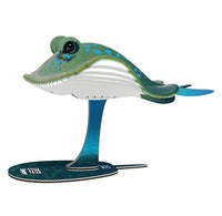A 3D cardboard model of a stingray on a stand, featuring a green and blue spotted dorsal side, a white underbelly, and a blue-tinted stand and base, shown against a plain white background.