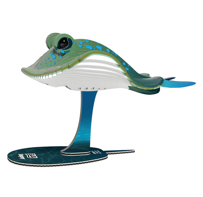 A 3D cardboard model of a stingray on a stand, featuring a green and blue spotted dorsal side, a white underbelly, and a blue-tinted stand and base, shown against a plain white background.