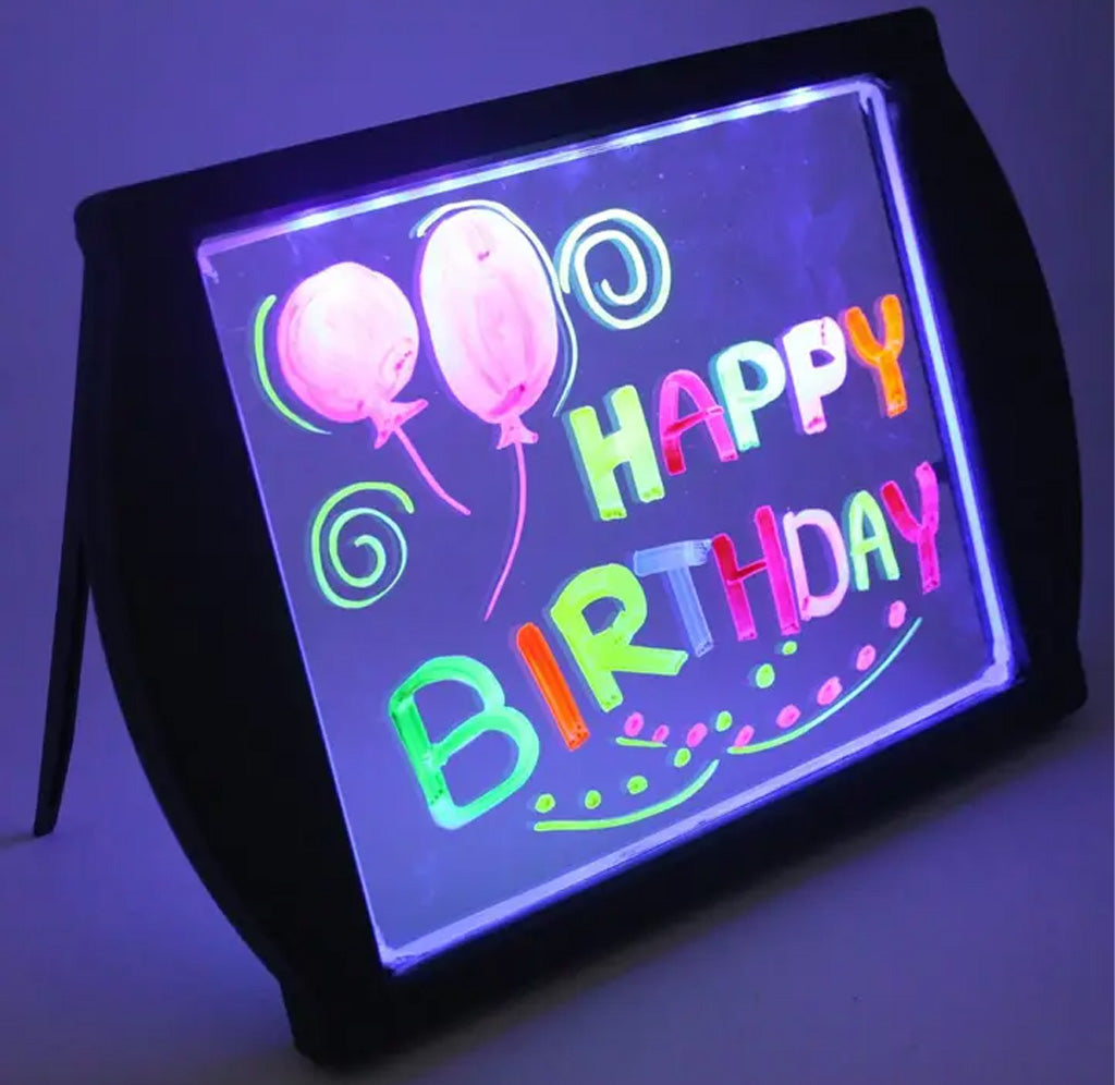 Glowing LED sign with 'Happy Birthday' text and balloons on a black stand against a dark background.