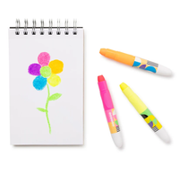 A childlike rainbow flower drawn in crayon on a spiral sketchbook, with orange, pink, and yellow crayons beside it; a bright, playful art scene.