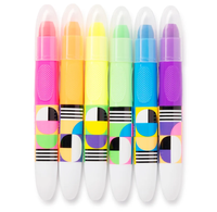 Six colorful tempera paint sticks stand in a row, with translucent caps and bright pink, orange, yellow, green, blue, and purple barrels decorated with playful geometric patterns. The image feels cheerful and vibrant.