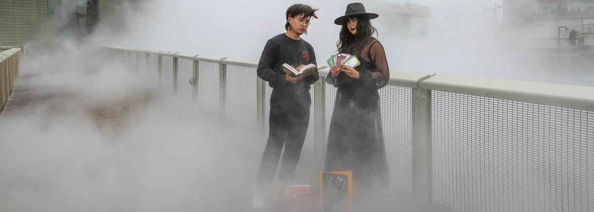 Two people stand on the Exploratorium Fog Bridge holding Halloween products