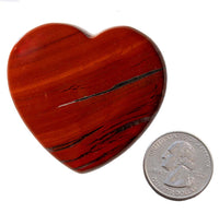 A red stone caved into the shape of a heart next to a quarter on a white background