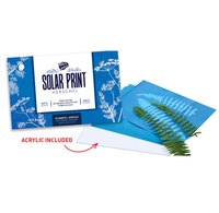 Herschel Solar Print acrylic art paper set with blue patterned packaging, a stack of blue sheets, a white sheet labeled acrylic included, and a green fern leaf on a white background.