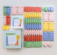 A colorful interlocking blocks set arranged on a light neutral background, including multiple pastel and bright wedge-shaped pieces, two instruction boxes, and several loose circular and interlocking pieces.