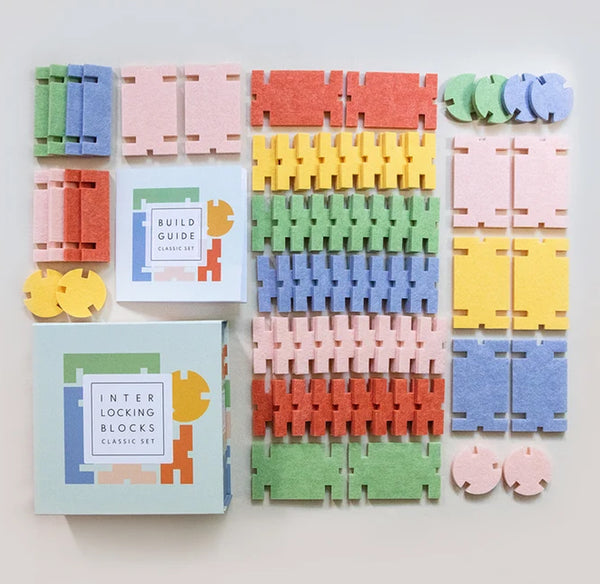 A colorful interlocking blocks set arranged on a light neutral background, including multiple pastel and bright wedge-shaped pieces, two instruction boxes, and several loose circular and interlocking pieces.