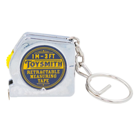 A small silver Toysmith retractable measuring tape with a blue-and-yellow label marked “1 m–3 ft,” attached to a metal key ring; practical, compact design.