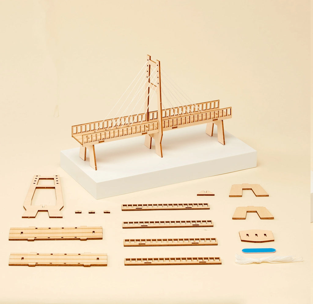Wooden bridge building kit with assembled model on a white base and multiple loose wooden pieces arranged on a beige background.