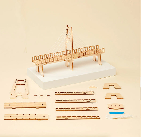 Wooden bridge building kit with assembled model on a white base and multiple loose wooden pieces arranged on a beige background.