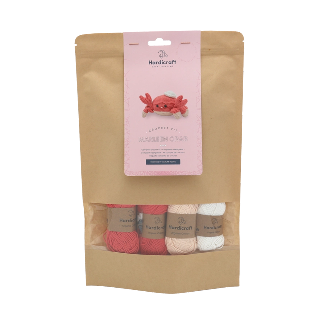 A Hardicraft crochet kit in a kraft paper pouch, with pink, coral, cream, and white yarn and a label featuring a cheerful crocheted crab.