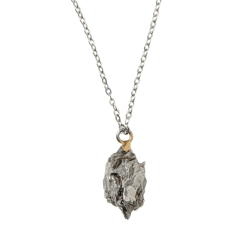 A small chunk of silver stone has a jump ring welded to the top to form a pendant. The pendant is hanging off a silver chain. 