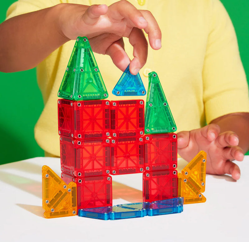 Child playing with colorful magnetic building blocks on a white surface with a green background