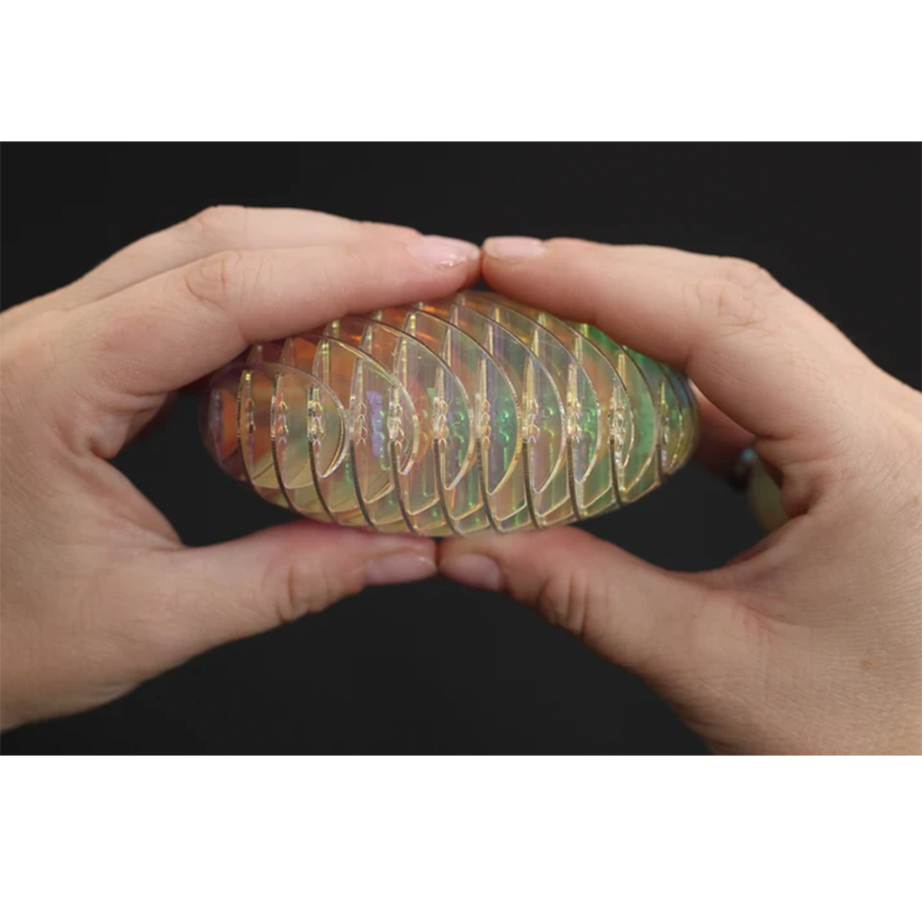 Two hands gently hold a translucent, rainbow-hued spiral shell-like object against a black background, creating a curious, tactile mood.