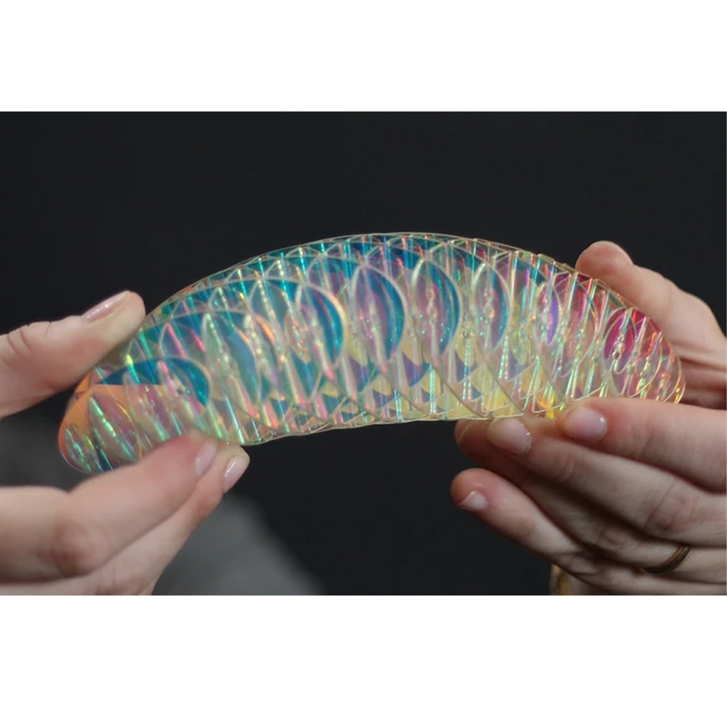 A person holds a curved, iridescent, holographic plastic item with a textured, ribbed surface against a dark background.
