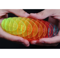 A close-up of hands holding a curved row of translucent plastic paddle blades in a rainbow gradient from green and yellow to orange, red, and blue, against a black background.