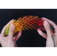 A pair of hands holding and stretching a translucent, flexible grid-like toy or accessory that shifts through green, yellow, orange, and red tones against a black background.
