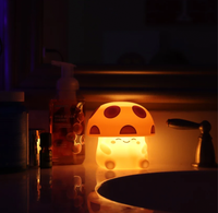 A smiling mushroom-shaped night-light glows orange on a dark bathroom counter beside soap bottles and a sink, creating a warm, cozy atmosphere.