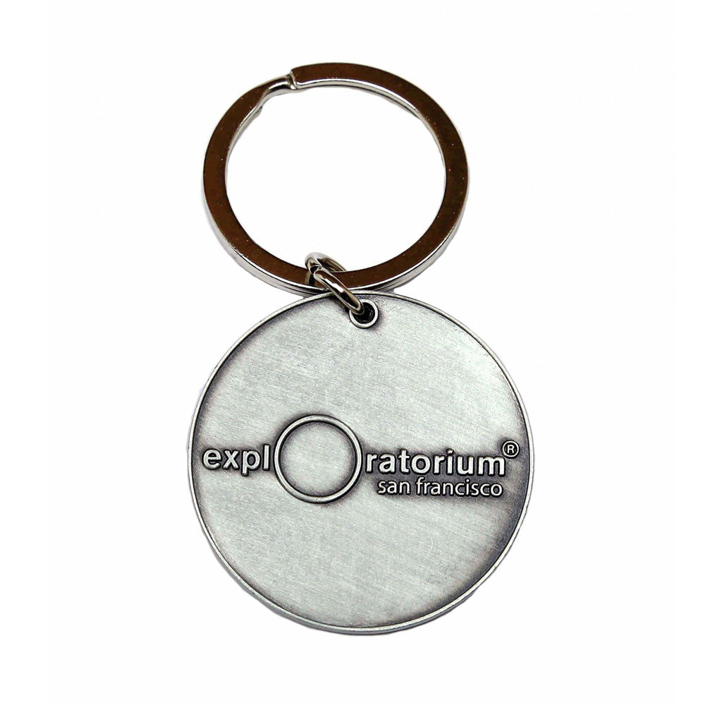 Circular metal pendant with the "Exploratorium" logo stamped on the back. Pendant is attached to a circular keyring. 
