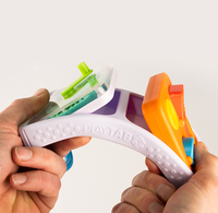 Hands stretch a flexible white PLAYTAB toy with bright green, orange, and blue components against a plain background, suggesting playful, hands-on fun.