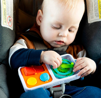 A focused baby sits safely in a car seat, exploring a colorful toy with gears and buttons; the close-up feels calm and curious.