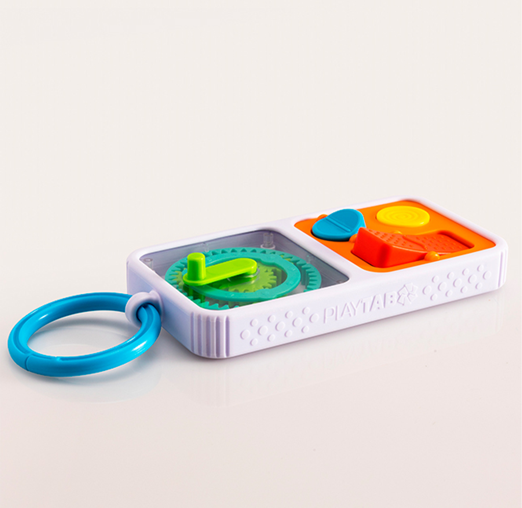 White rectangular baby toy with a blue handle, green spinning gear, and orange-and-yellow textured buttons, photographed on a pale background; playful and soothing.